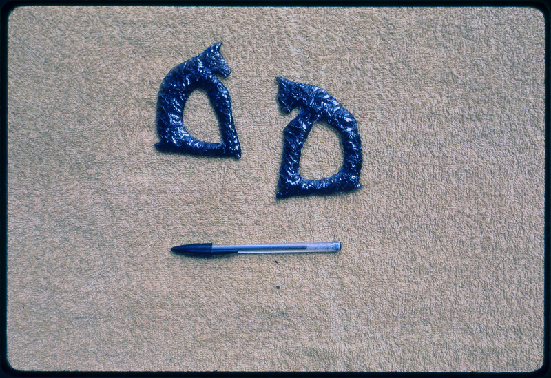 A photographic slide of two obsidian artifacts depicting the facade of a dog and a cat respectively.