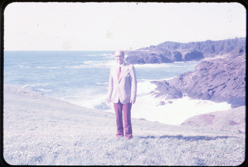 A photographic slide of Don E. Crabtree standing in front of a rocky beach.