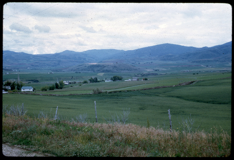 A photographic slide of a grassy field in front of a series of foothills.