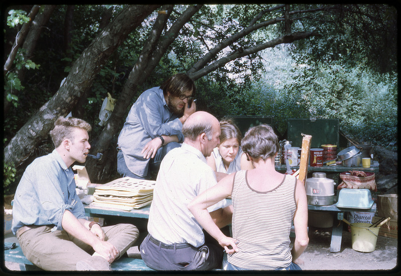 A photographic slide of a group of people gathered on a park bench over an unknown item.