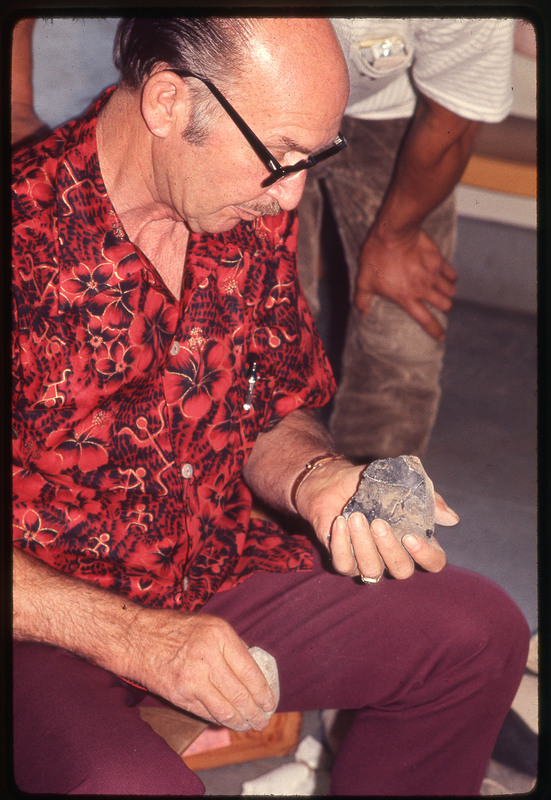 A photographic slide of Don E. Crabtree flintknapping with obsidian while seated inside.