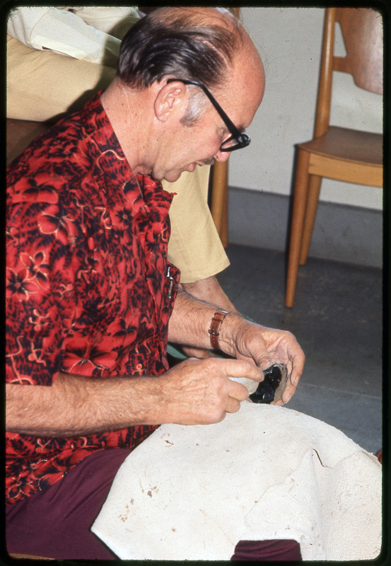 A photographic slide of Don E. Crabtree flintknapping with obsidian while seated inside.