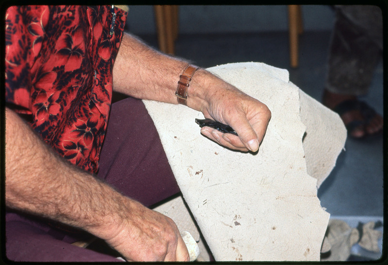 A photographic slide of Don E. Crabtree flintknapping with obsidian while seated inside.