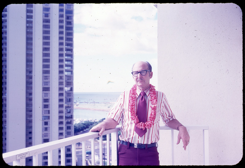 A photographic slide of Don E. Crabtree smiling on a balcony, wearing a floral lei necklace.