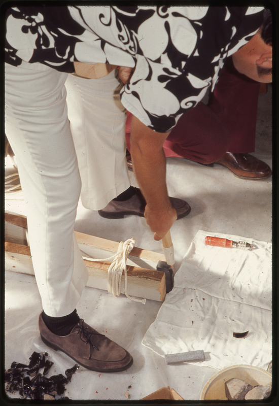 A photographic slide of a man using a chest crutch to flintknap.