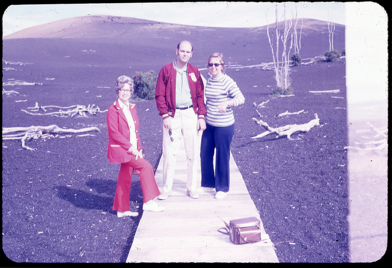 A photographic slide of three people posing in front of dark sand flats.