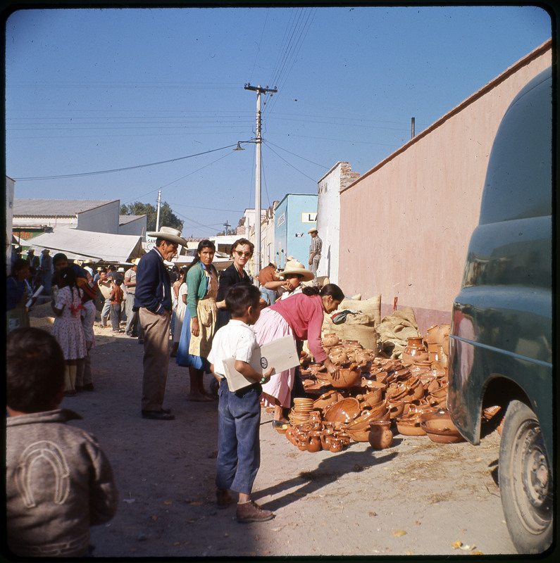 A photographic slide displaying a group of people standing next to a large pile of assorted ceramics. A few of them are inspecting the wares.