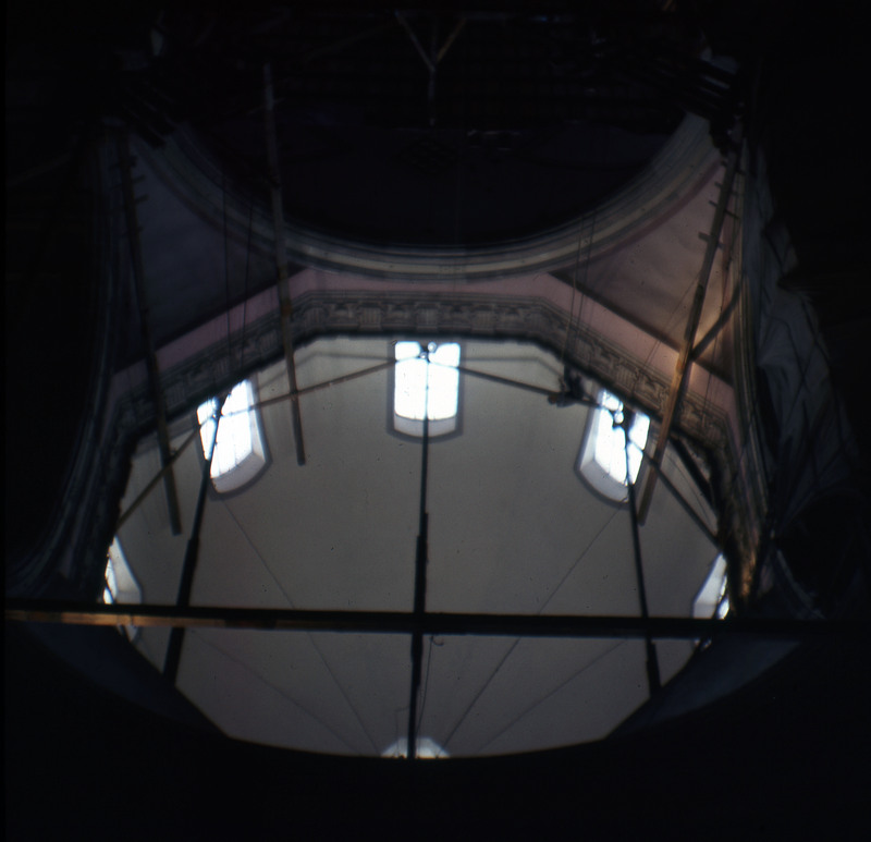 A photographic slide displaying an interior shot of a cathedral's dome. Its perimeter is dotted by windows, and large wooden beams are aligned horizontally and vertically within. The entire slide is tinted red.