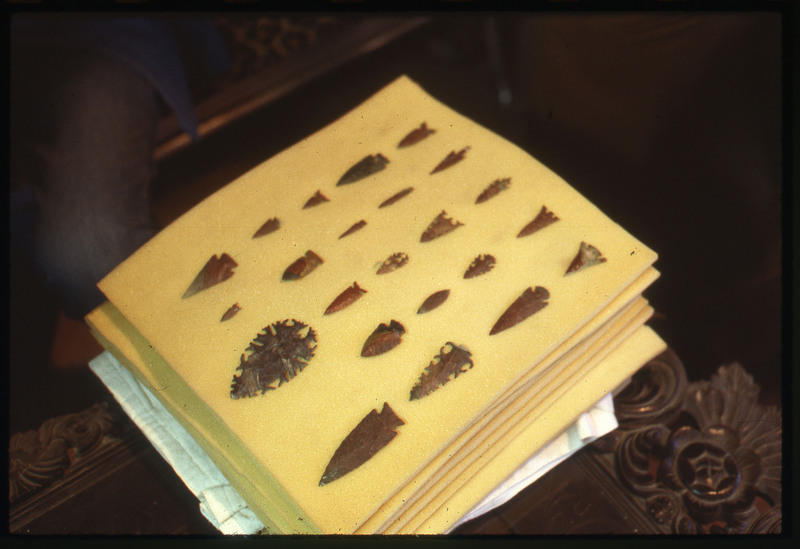 A photographic slide of an arrangement of uniquely flintknapped bifaces. They are neatly organized and most appear to be arrowheads.