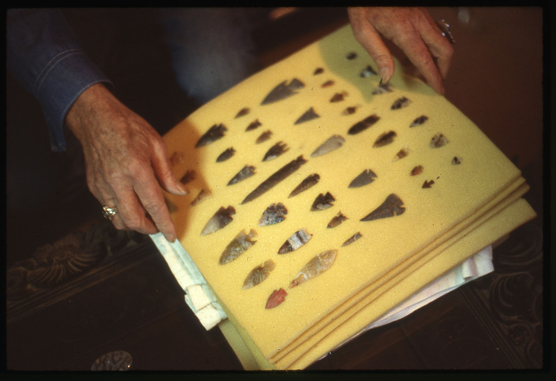 A photographic slide of an arrangement of flintknapped bifaces. They appear to be arrowheads and they are neatly organized.