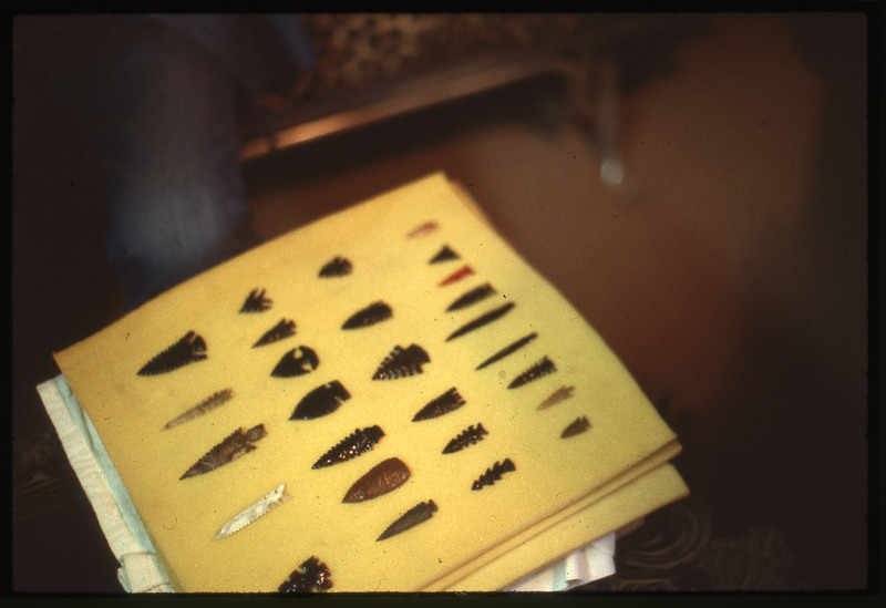 A photographic slide of an arrangement of flintknapped bifaces that are arrowheads. They are neatly arranged and all different.