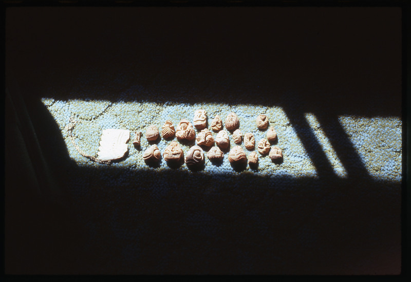 A photographic slide of multiple wooden carved faces. They are on the carpet and pictured in a sliver of sunlight.