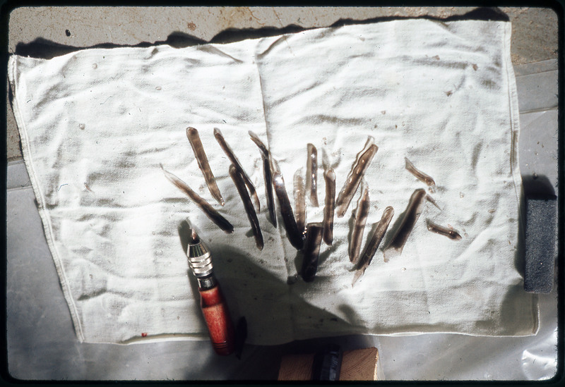 A photographic slide of flintknapped flakes. They are long vertical flakes on a rag. There is also a copper tipped tool pictured.