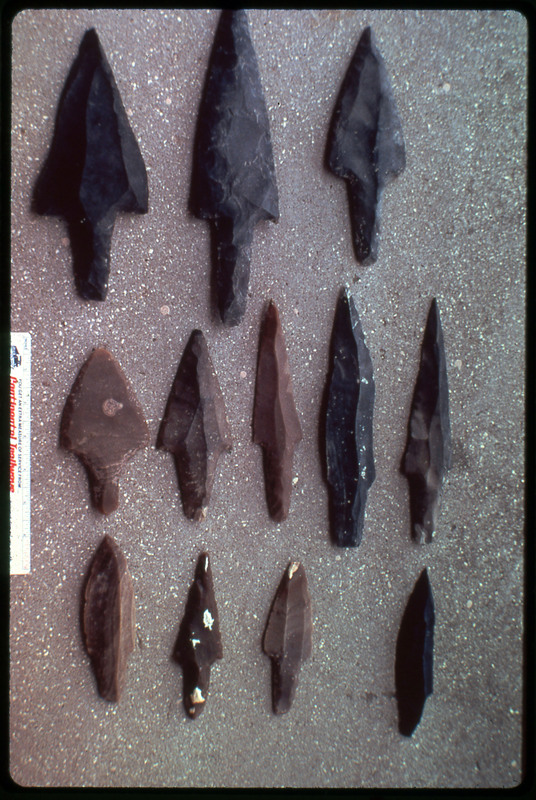 A photographic slide of arrowheads arranged in a neat formation. There are twelve arrowheads.