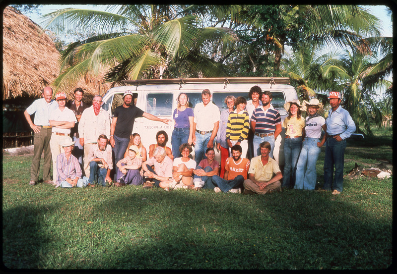 A photographic slide of a large group of people posed together outside a van. There are palm trees in the background.