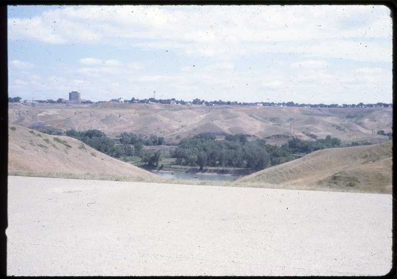 A photographic slide of a valley with a river. There is a city on top of the hill above the river.