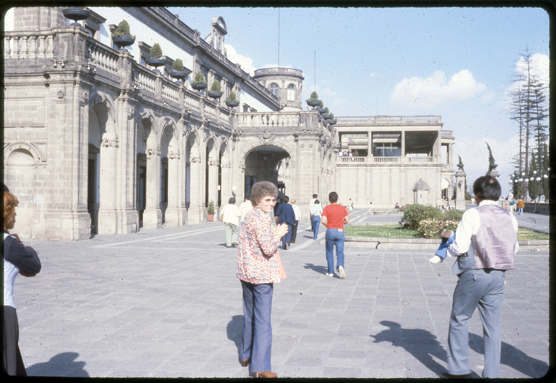 A photographic slide of people, with the camera focused on one woman, going into a nice building. This might be the museum of anthropology.