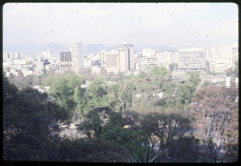 A photographic slide of a cityscape with many trees in the foreground.