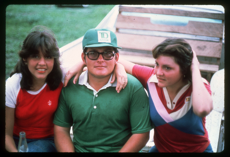 A photographic slide of a boy in green and town young girls in red sitting outside on a truck bed together.