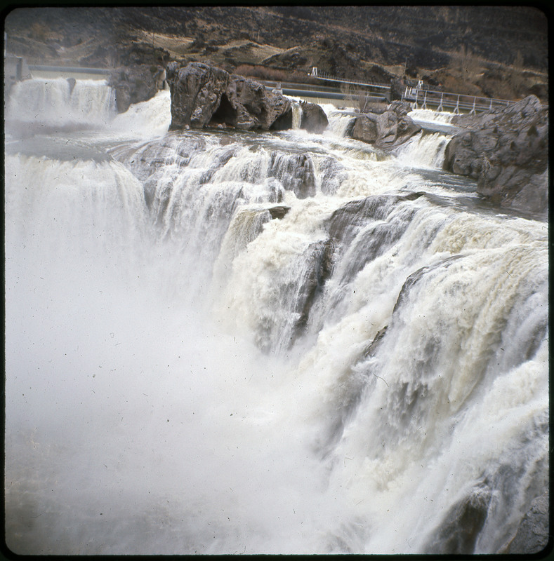 A photographic slide of a waterfall. There is a large rush of mist and many large boulders.