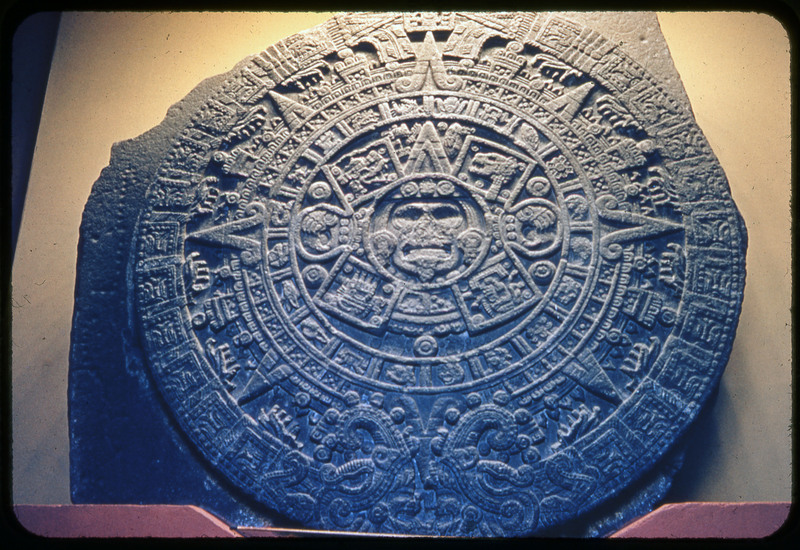 A photographic slide of what resembles an Aztec stone carving artifact. There is a face in the center and various detailed patterns encircling it.