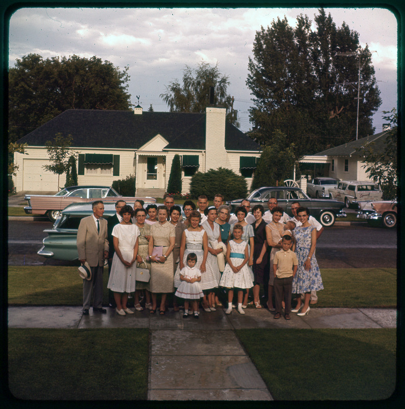 A photographic slide of a large group of people standing together outside on a neighborhood street. There are cars on the road and houses in the background. There are many people and children.