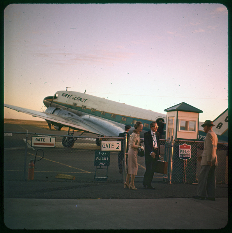 A photographic slide of three people standing at airport gates. There are planes in the background on the tarmac.