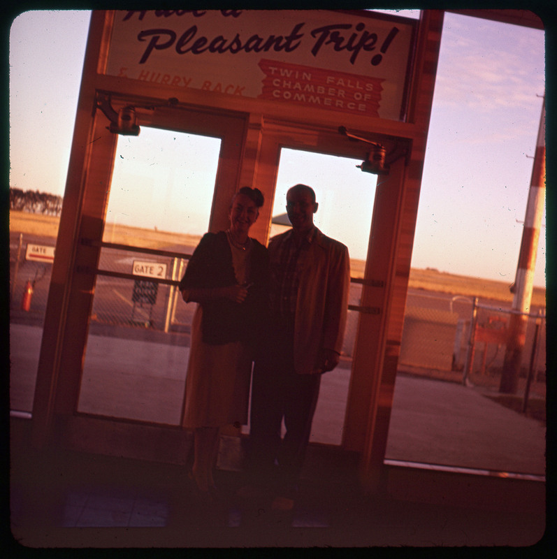 A photographic slide of Donald and Evelyn Crabtree standing together at an airport. They are at a door and there are fenced gates in the background.