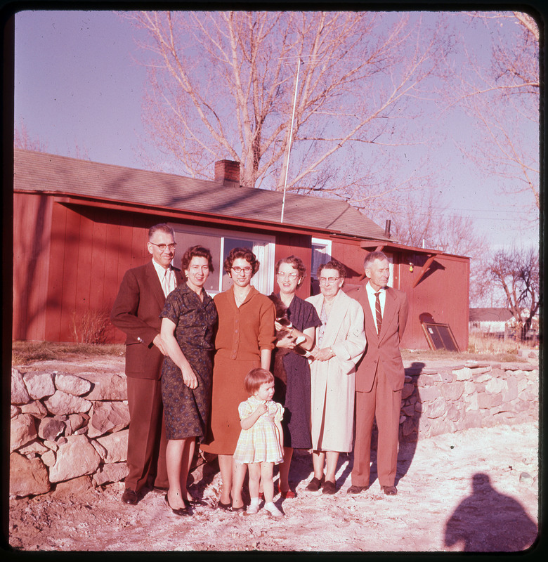 A photographic slide of Evelyn Crabtree and who are presumed to be her family. Evelyn Crabtree is holding a cat. They are standing in front of a red house.