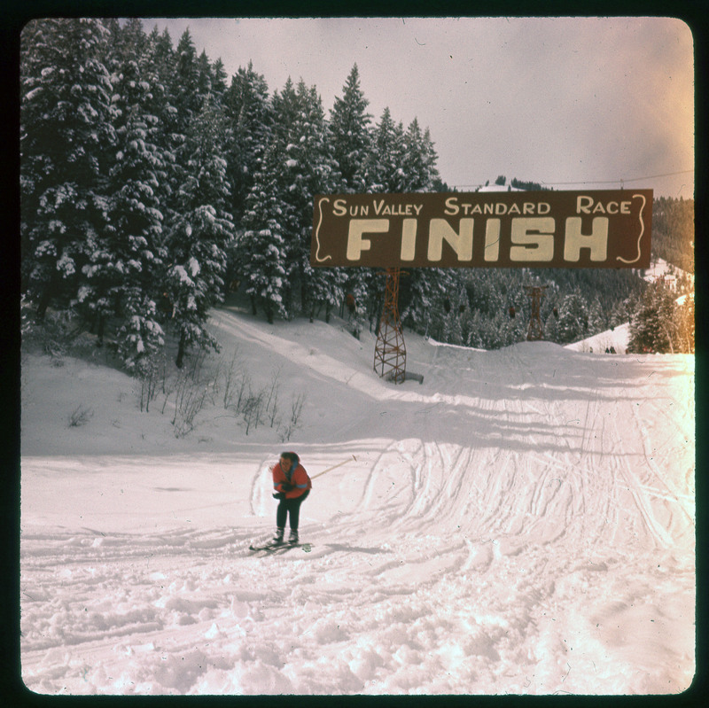 A photographic slide of a person skiing past a race finish line. This is for the Sun Valley Standard Race.