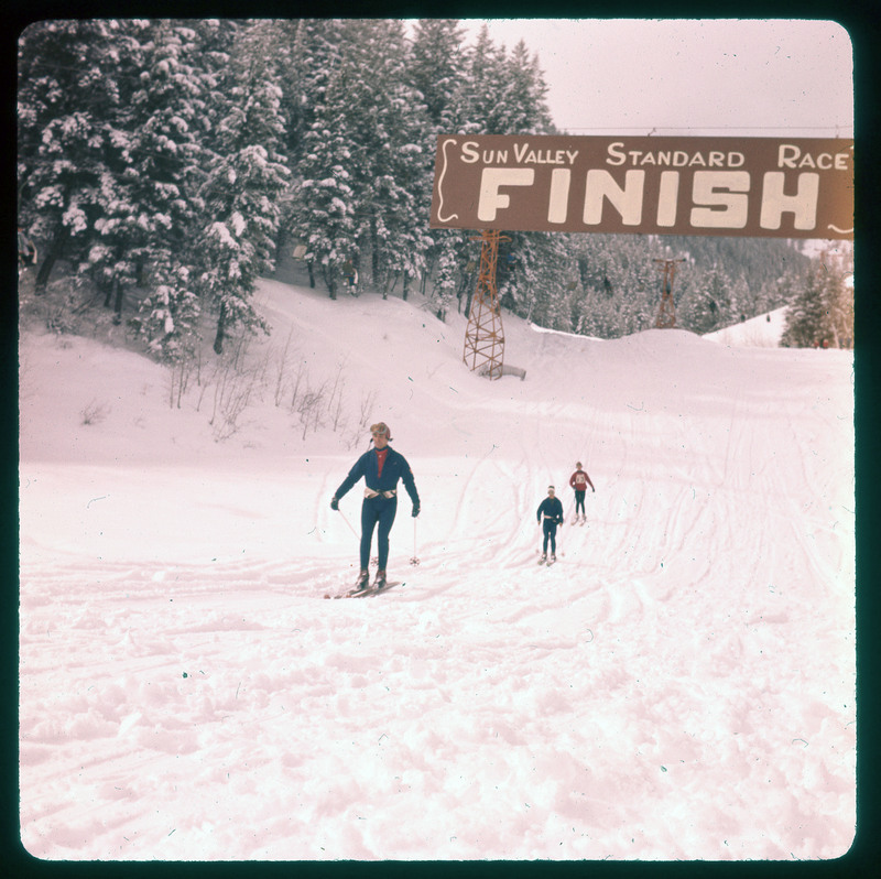 A photographic slide of three people crossing a finish line for a skiing race.