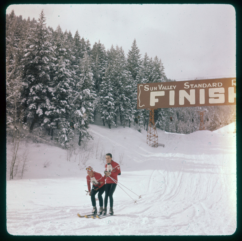 A photographic slide of a skiing race finish line. There are two smiling people who just finished.