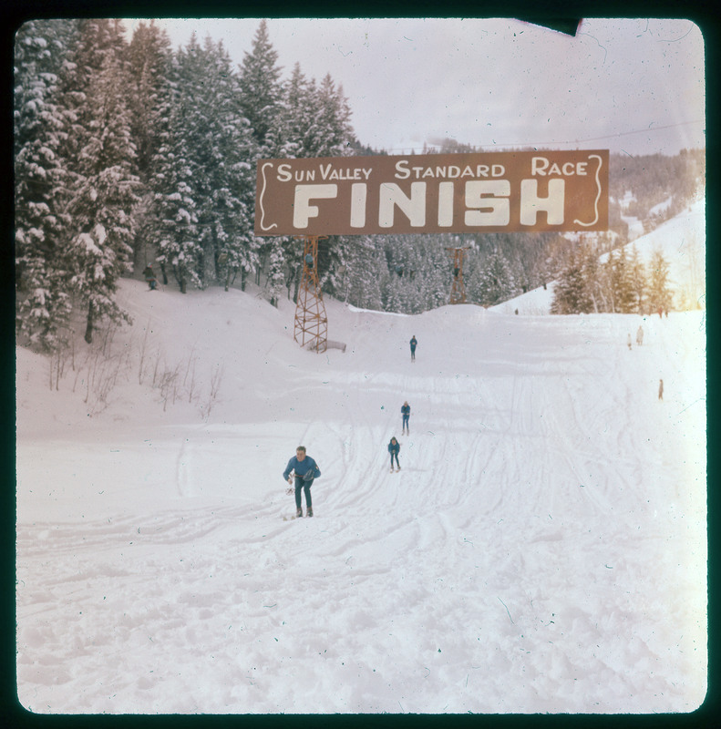 A photographic slide of people crossing a skiing race finish line. This is for the Sun Valley Standard Race.