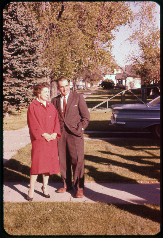 A photographic slide of a couple standing outside on a sidewalk. There are houses and a car in the background.