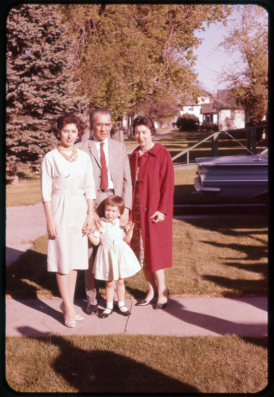 A photographic slide of a family standing outside on an sidewalk together. There are four people and houses in the background.