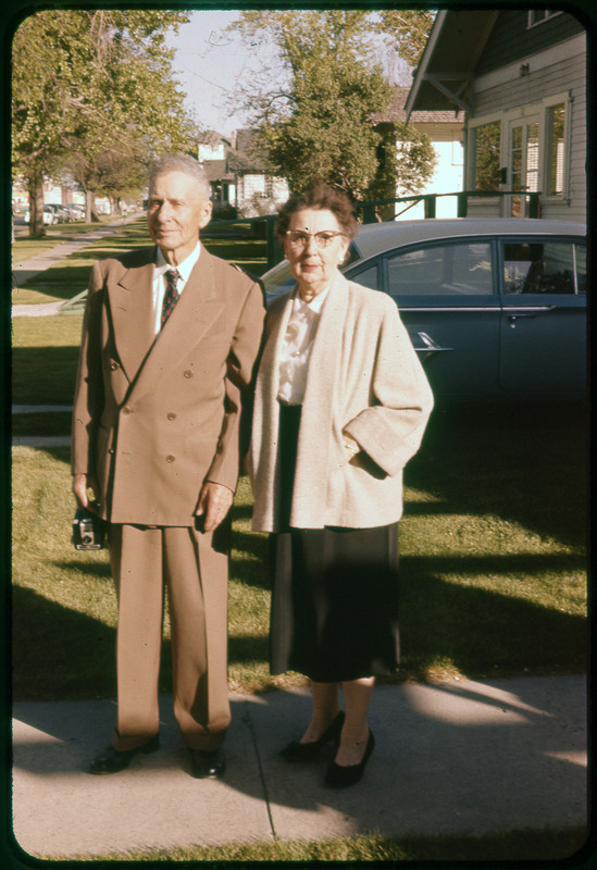 A photographic slide of a couple standing on the sidewalk outside together. There is a car parked behind them.