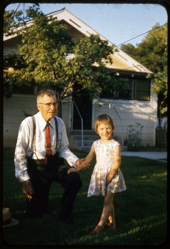 A photographic slide of a child with an older man holding their hand on an front lawn in front of a house.