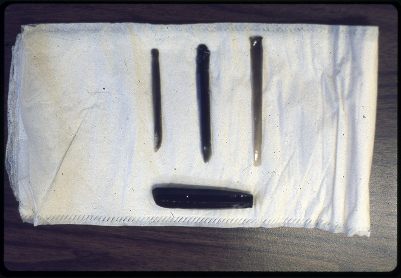 A photographic slide of four flintknapped materials. They are long vertical shards on a cloth.