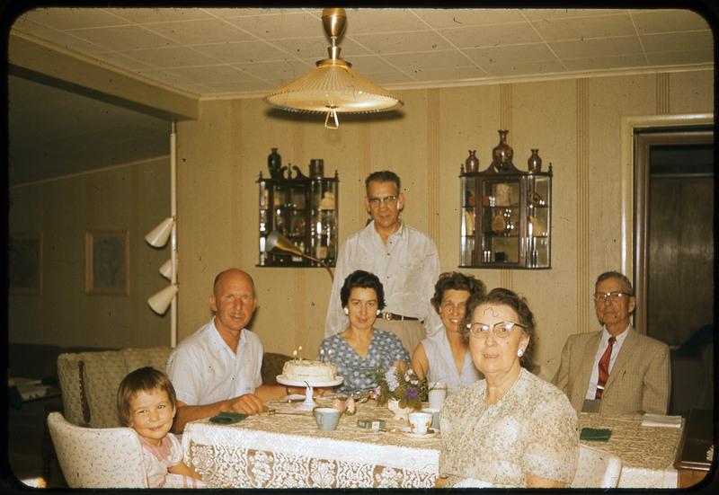 A photographic slide of seven people, including Donald Crabtree, sitting at a table together around a birthday cake. The cake is in front of Crabtree.