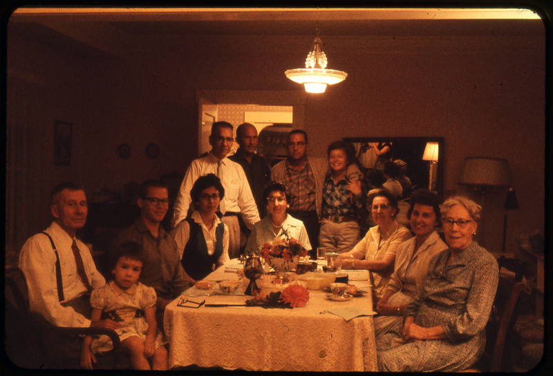 A photographic slide of a large group of people sitting at a dinner table together. The table is nicely set. This photo is a similar version to ce.81.25.24.