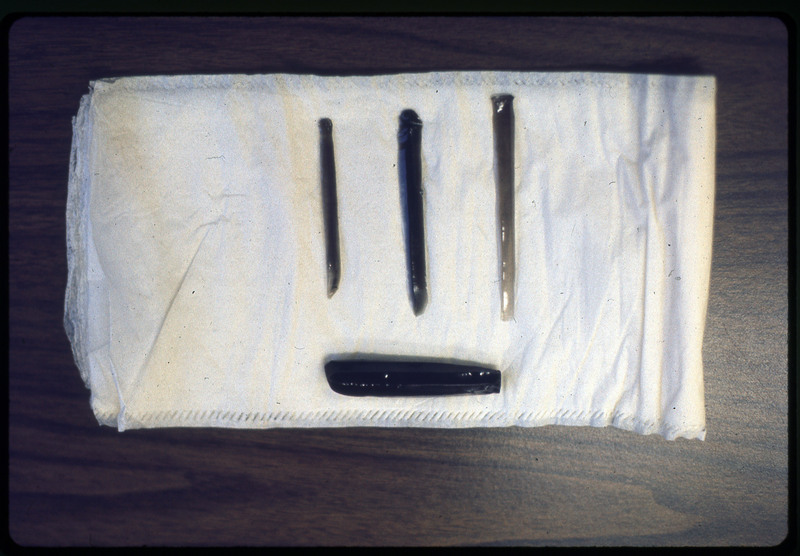 A photographic slide of four flintknapped materials on a white cloth. The flakes are long and vertical.