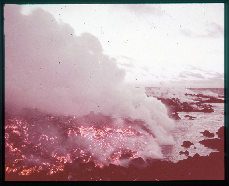 A photographic slide of a large lava flow next to water. There is steam coming off the lava.