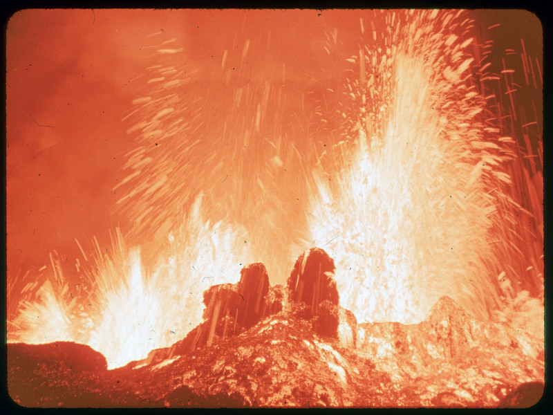 A photographic slide of a lot of lava spewing into the air among lava rock.