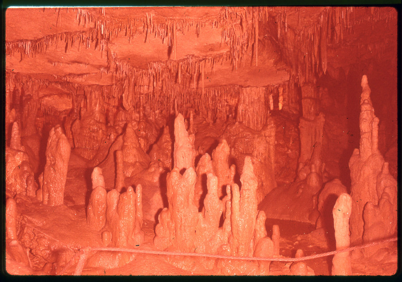 A photographic slide of stalagmites and stalactites in a cave with a railing.