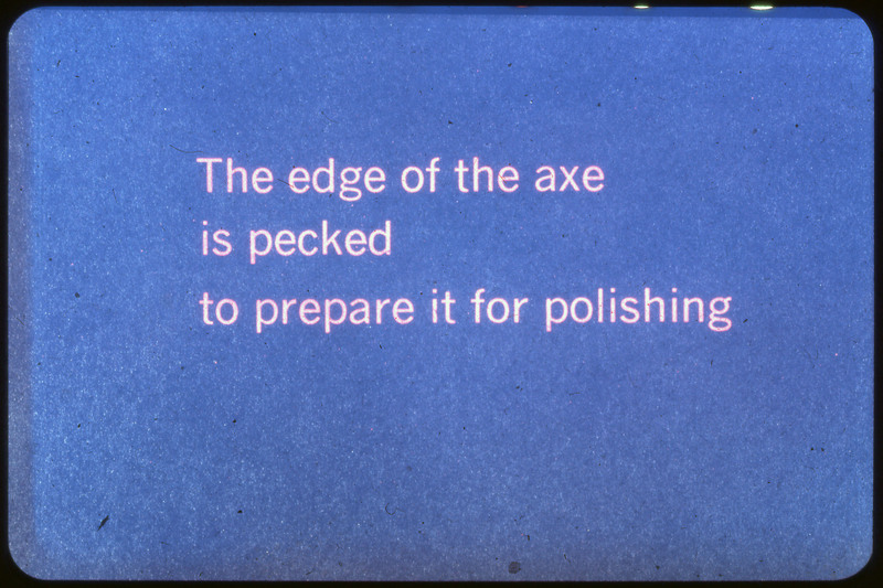 A photographic slide of a blue slide stating, "The edge of the axe is pecked to prepare it for polishing."