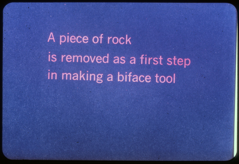 A photographic slide of a blue slide stating, "A piece of rock is removed as a first step in making a biface tool."