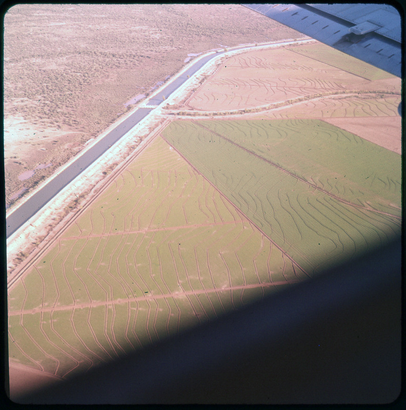 A photographic slide of grassy farmland fields from an aerial view. There is what resembles a road or a river visible.