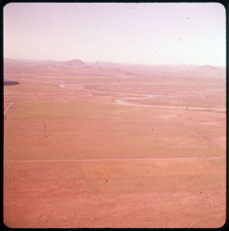 A photographic slide of farmland and a winding river. There are mountains in the background.