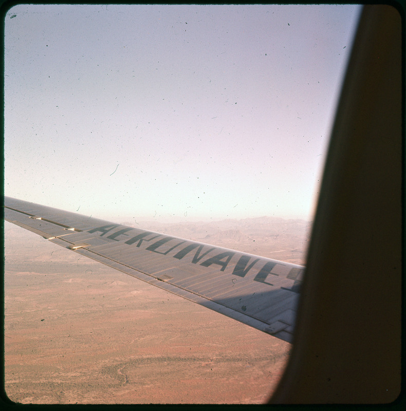 A photographic slide of the wing of an airplane. There is an aerial view of farmland in the background.