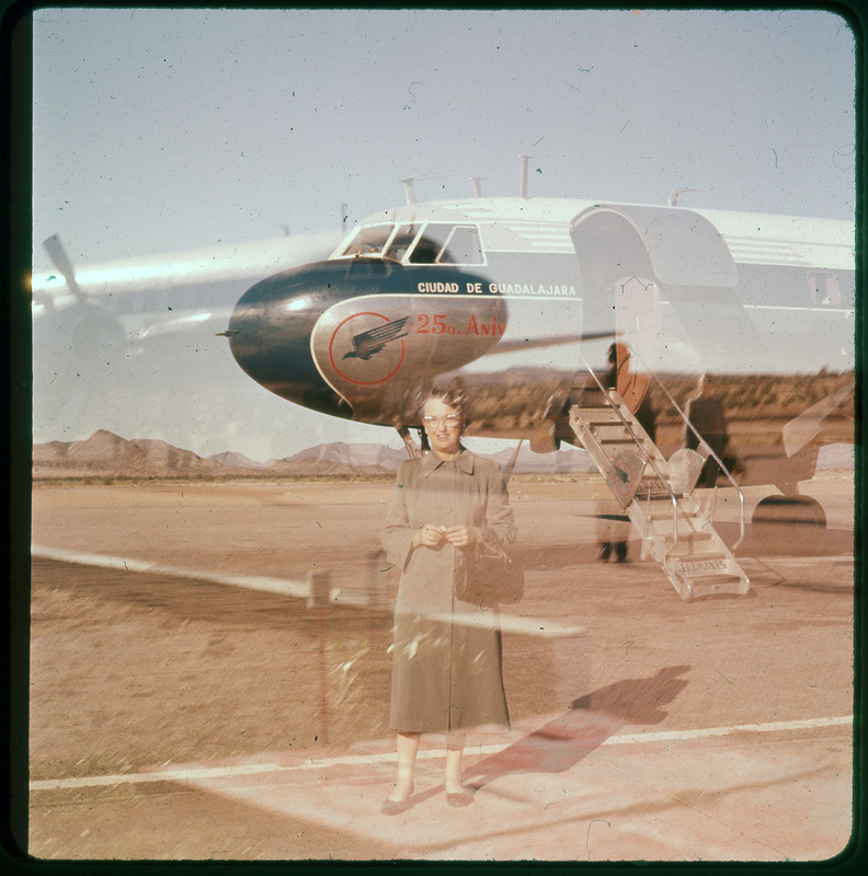 A photographic slide of Evelyn Crabtree in front of a plane. The photo developed incorrectly and it is blurry with an image of another plane and other people.